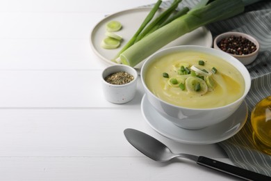 Bowl of tasty cream soup with leek and spoon on white wooden table. Space for text