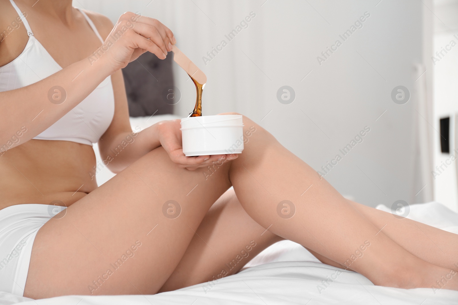 Photo of Woman holding hot wax on bed at home, closeup. Epilation procedure