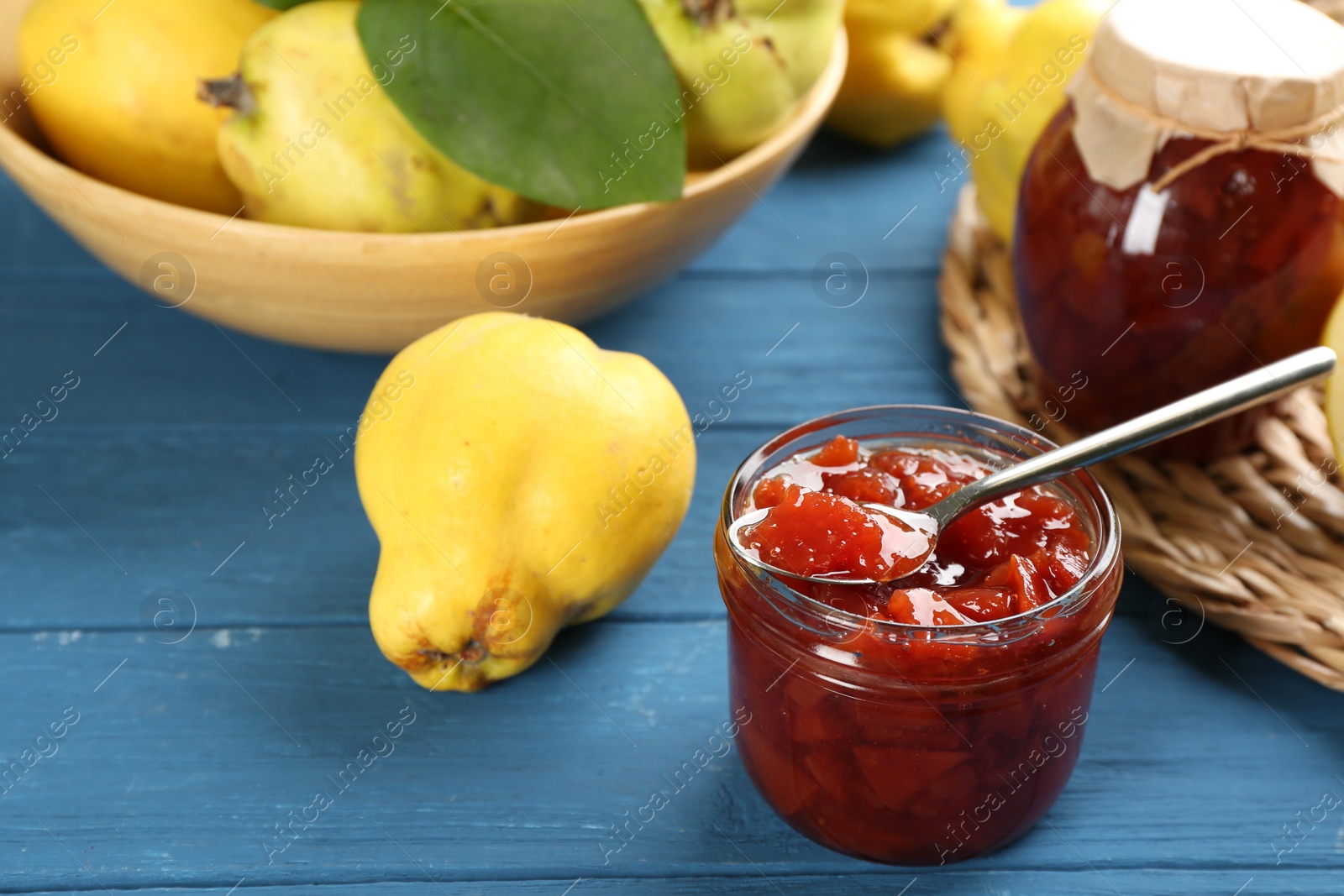 Photo of Delicious quince jam and fruit on blue wooden table, closeup