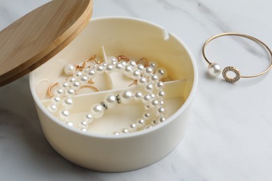 Stylish jewelry with pearls in box on white marble table, closeup view