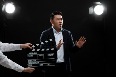 Photo of Emotional asian actor performing while second assistant camera holding clapperboard on stage. Film industry