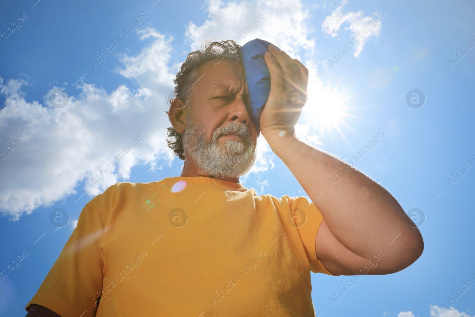 Photo of Senior man with cold pack suffering from heat stroke outdoors, low angle view