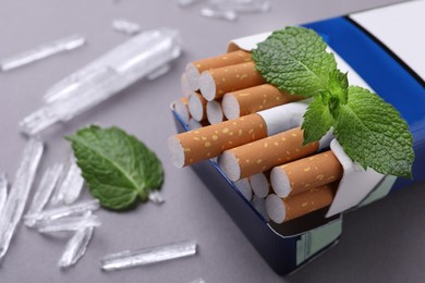 Photo of Pack of cigarettes, menthol crystals and mint leaves on grey background, closeup