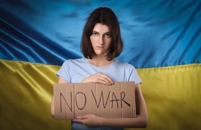 Sad woman holding poster with words No War near Ukrainian flag