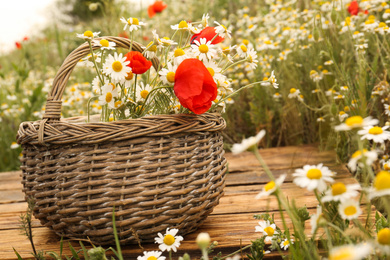 Photo of Bouquet of poppies and chamomiles in wicker basket on wooden table outdoors