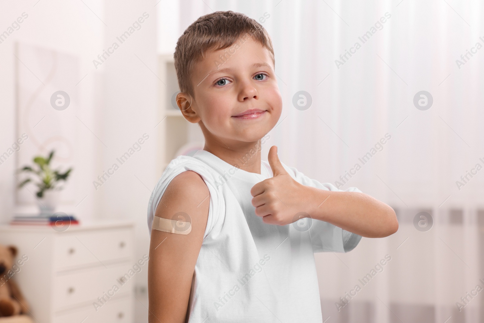 Photo of Boy with sticking plaster on arm after vaccination showing thumbs up indoors
