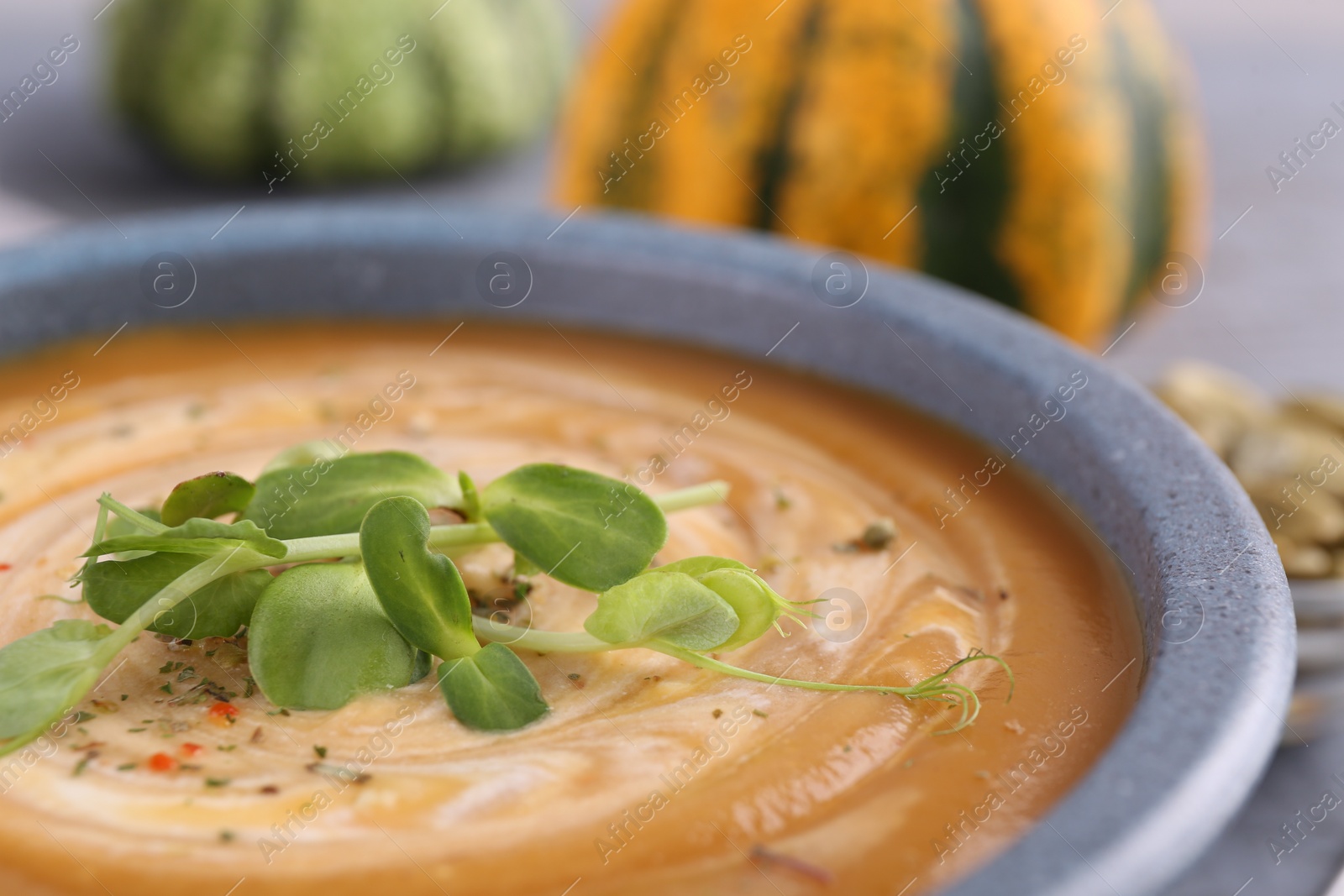 Photo of Tasty pumpkin soup with microgreens in bowl on table, closeup