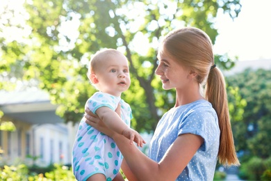 Teen nanny with cute baby outdoors on sunny day