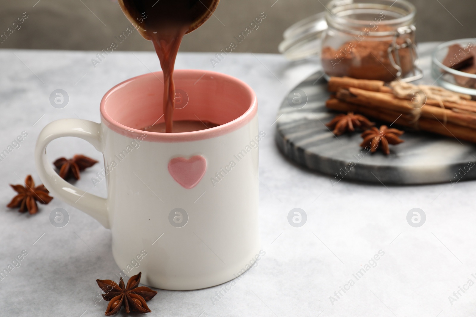 Photo of Pouring tasty hot chocolate into cup at light table, closeup. Space for text