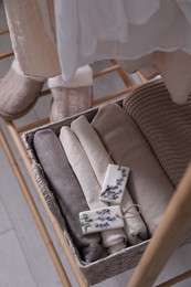 Beautiful scented wax sachets and folded clothes in wicker basket on rack indoors