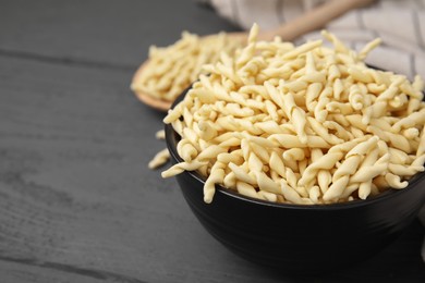 Uncooked trofie pasta in bowl on grey wooden table, closeup. Space for text
