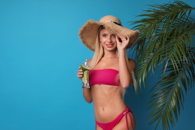 Pretty young woman wearing stylish bikini with cocktail on blue background. Space for text