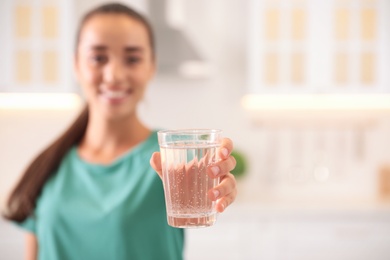 Photo of Young woman holding glass of pure water in kitchen, focus on hand