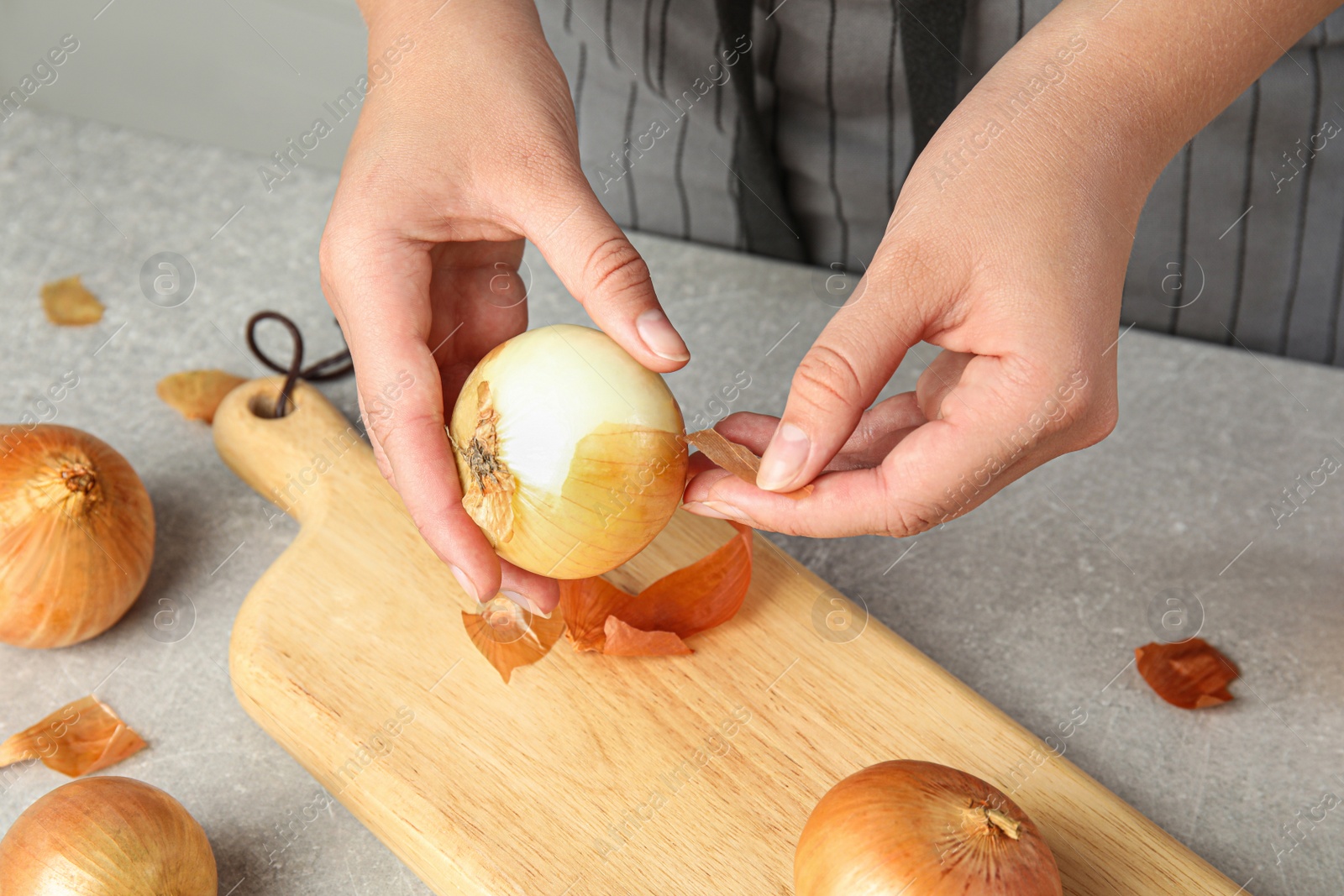 Photo of Young woman peeling ripe onion at grey table, closeup