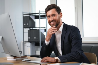 Photo of Smiling bearded man near computer at table in office