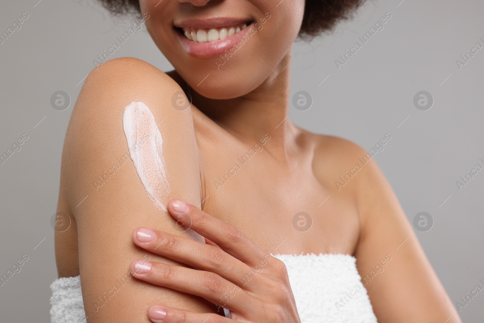 Photo of Young woman applying body cream onto shoulder on grey background, closeup