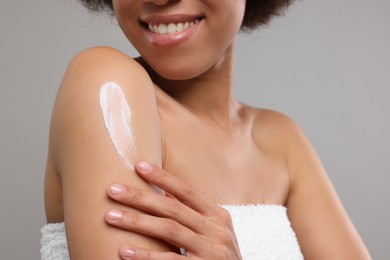 Young woman applying body cream onto shoulder on grey background, closeup