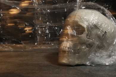 Human skull with stretch film on stone surface against black background. Space for text