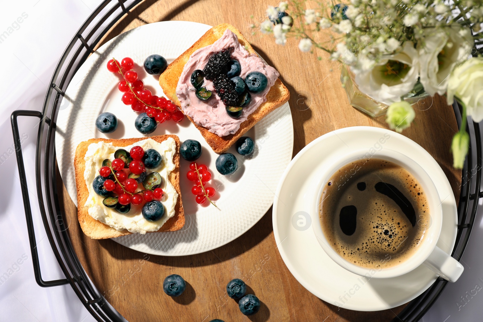 Photo of Tray with cup of coffee, cream cheese sandwiches and flowers on white fabric, top view