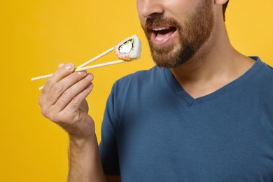 Man eating sushi roll with chopsticks on orange background, closeup