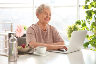 Photo of Elderly woman using laptop while having breakfast at home