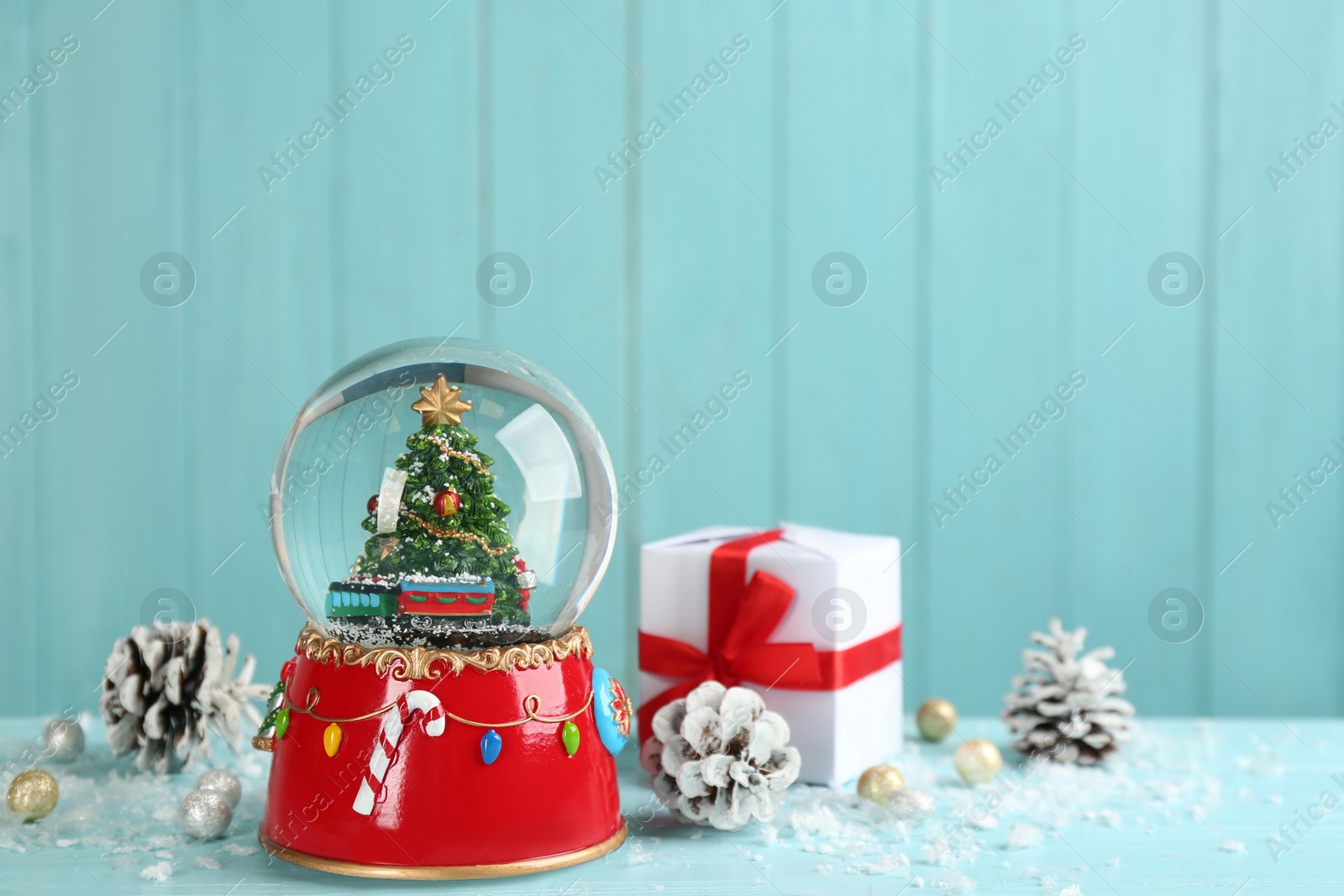 Photo of Beautiful snow globe, gift box and Christmas decor on light blue table, space for text