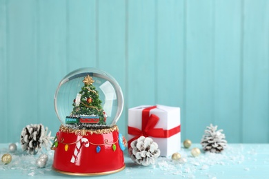 Beautiful snow globe, gift box and Christmas decor on light blue table, space for text