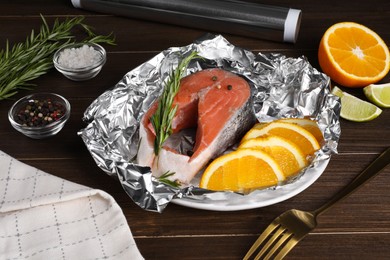 Photo of Aluminum foil, raw fish, orange and spices on wooden table