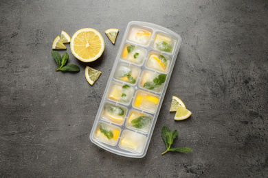 Ice cubes with lemon and mint in tray on grey table, flat lay