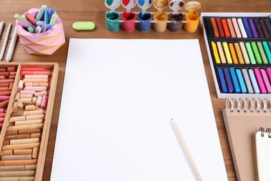 Photo of Blank sheet of paper, colorful chalk pastels and other drawing tools on wooden table. Modern artist's workplace