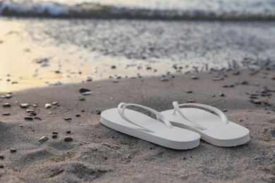 Stylish white flip flops on sand near sea. Space for text