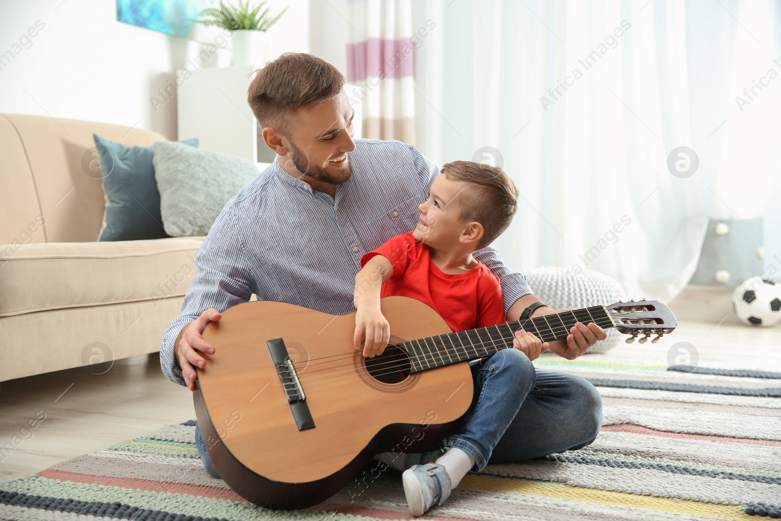 Photo of Father teaching his little son to play guitar at home