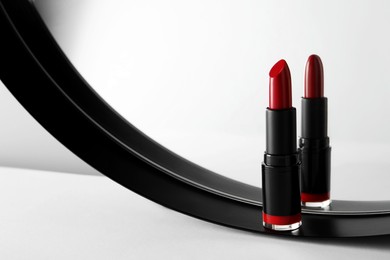 Stylish presentation of beautiful red lipstick and mirror on white table