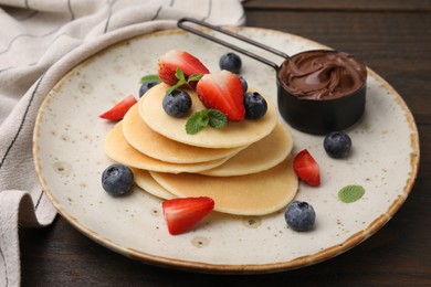 Photo of Delicious pancakes served with berries and chocolate spread on wooden table, closeup