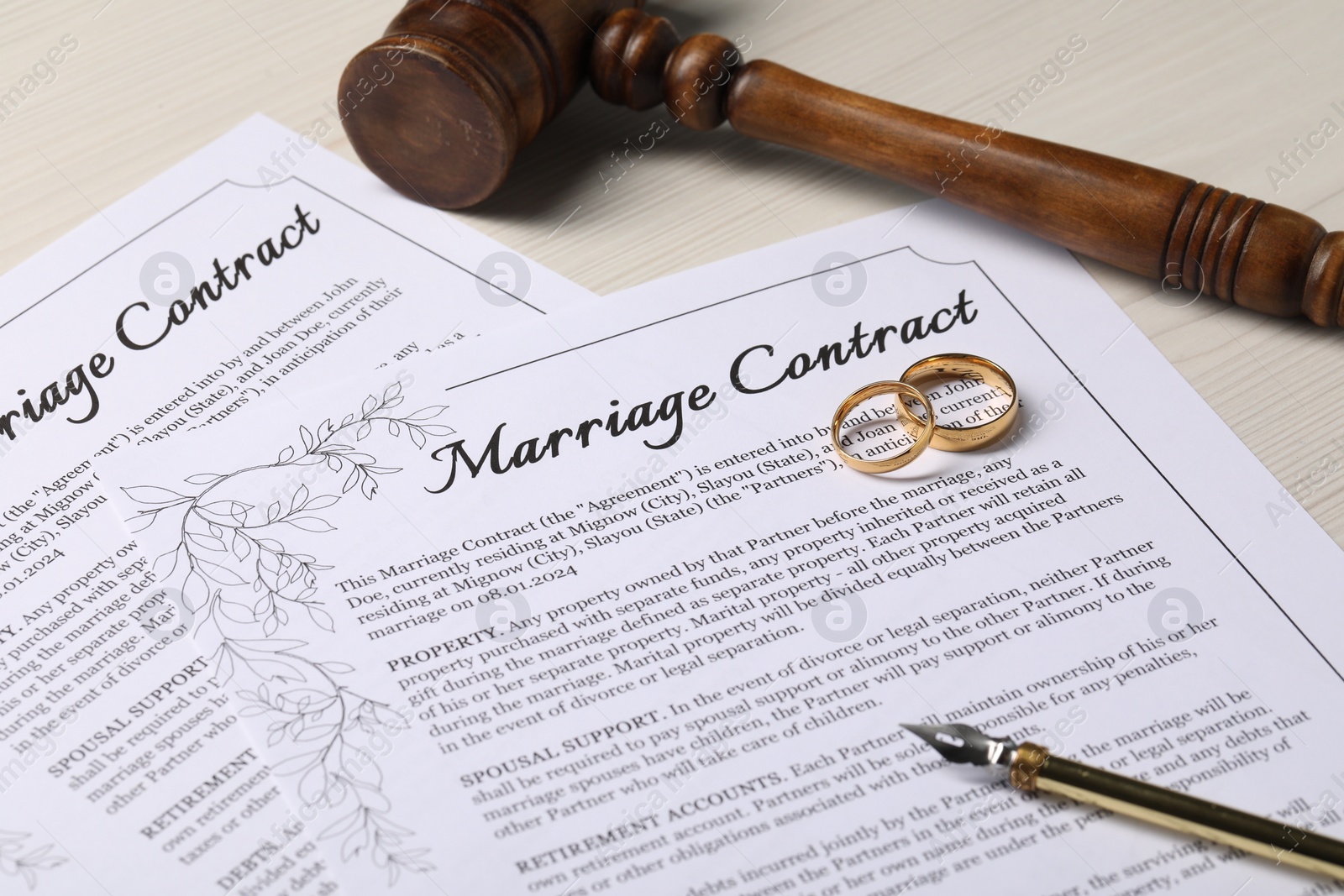 Photo of Marriage contracts, gold rings, pen and gavel on light wooden table, closeup