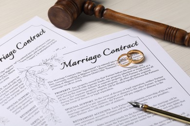 Marriage contracts, gold rings, pen and gavel on light wooden table, closeup