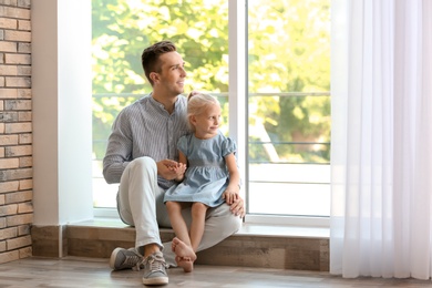 Photo of Young man with cute little girl near window at home