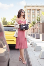 Photo of Young woman in sunglasses with stylish black bag on city street