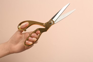 Woman holding sewing scissors on beige background, closeup