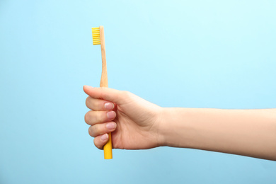 Woman holding bamboo toothbrush on light blue background, closeup