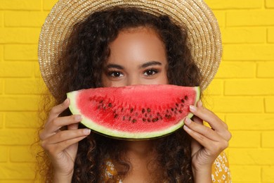 Photo of Beautiful young African American woman with watermelon near yellow brick wall