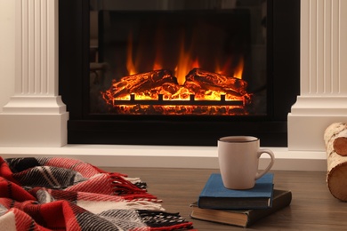 Photo of Cup of hot tea and books on floor near fireplace. Cozy atmosphere