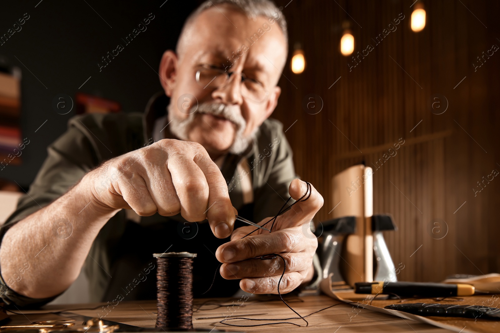 Photo of Man cutting thread while working with leather at table, focus on hands