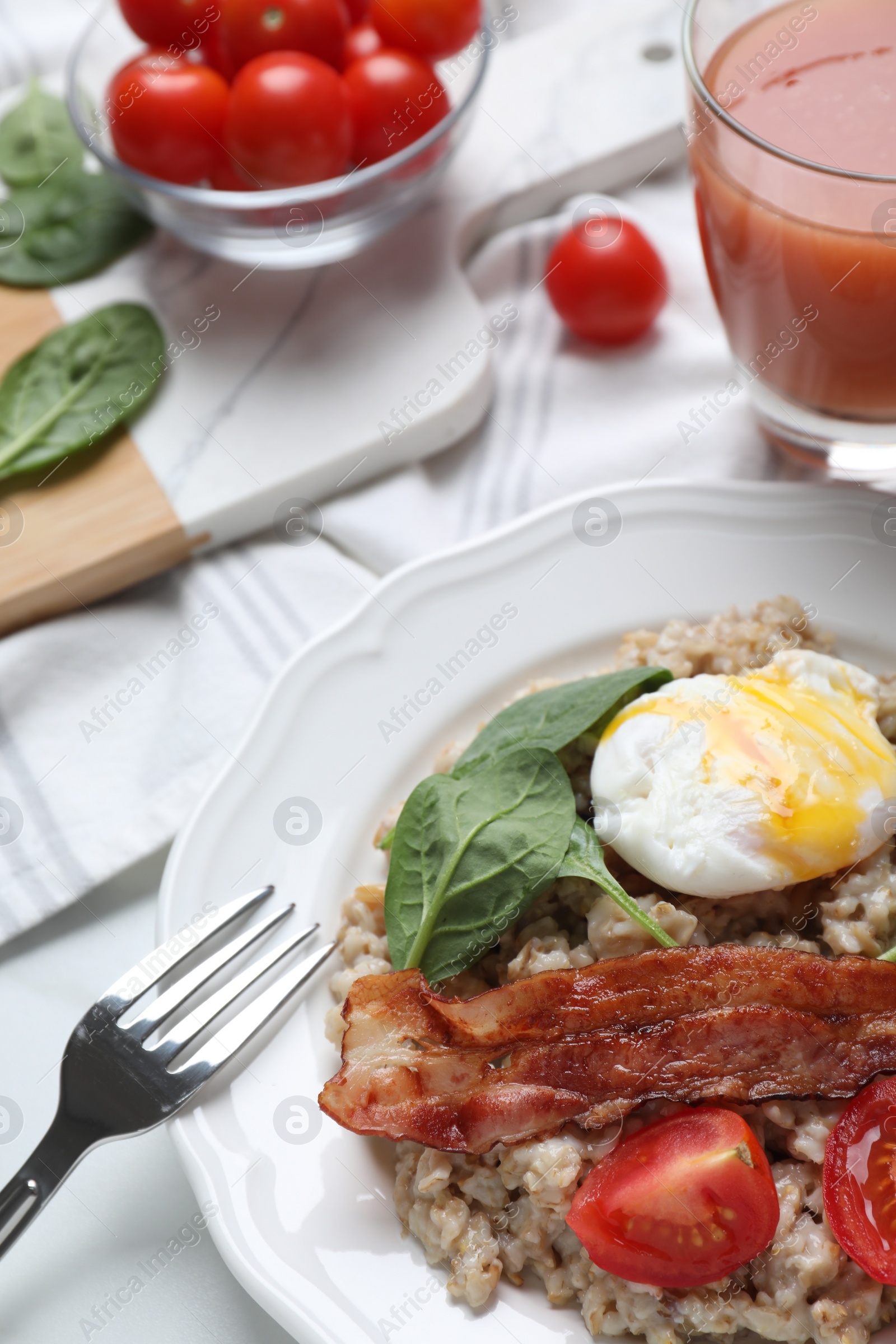 Photo of Delicious boiled oatmeal with poached egg, bacon and tomato served on table, closeup