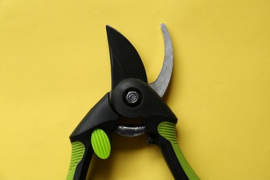 Secateur on light yellow background, top view