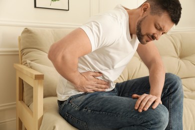 Photo of Man suffering from pain in lower right abdomen on sofa at home. Acute appendicitis