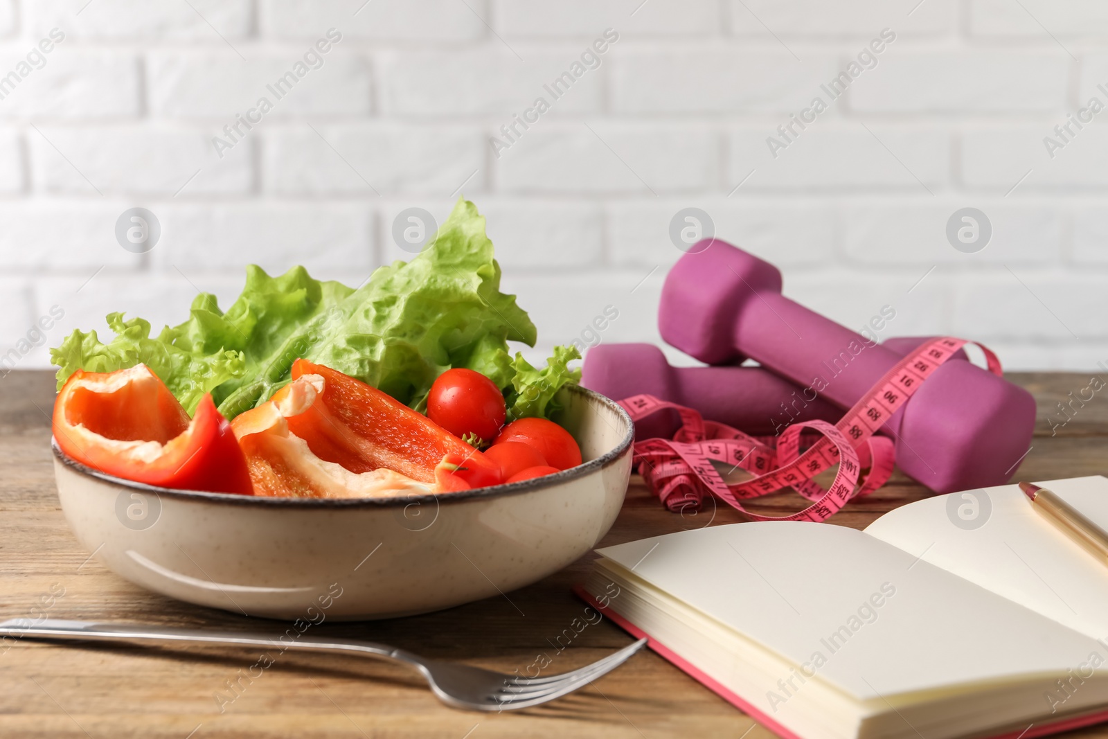 Photo of Healthy diet. Vegetables, fork, notebook, dumbbells and measuring tape on wooden table, closeup