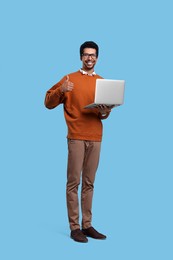 Photo of Happy man with laptop showing thumb up on light blue background