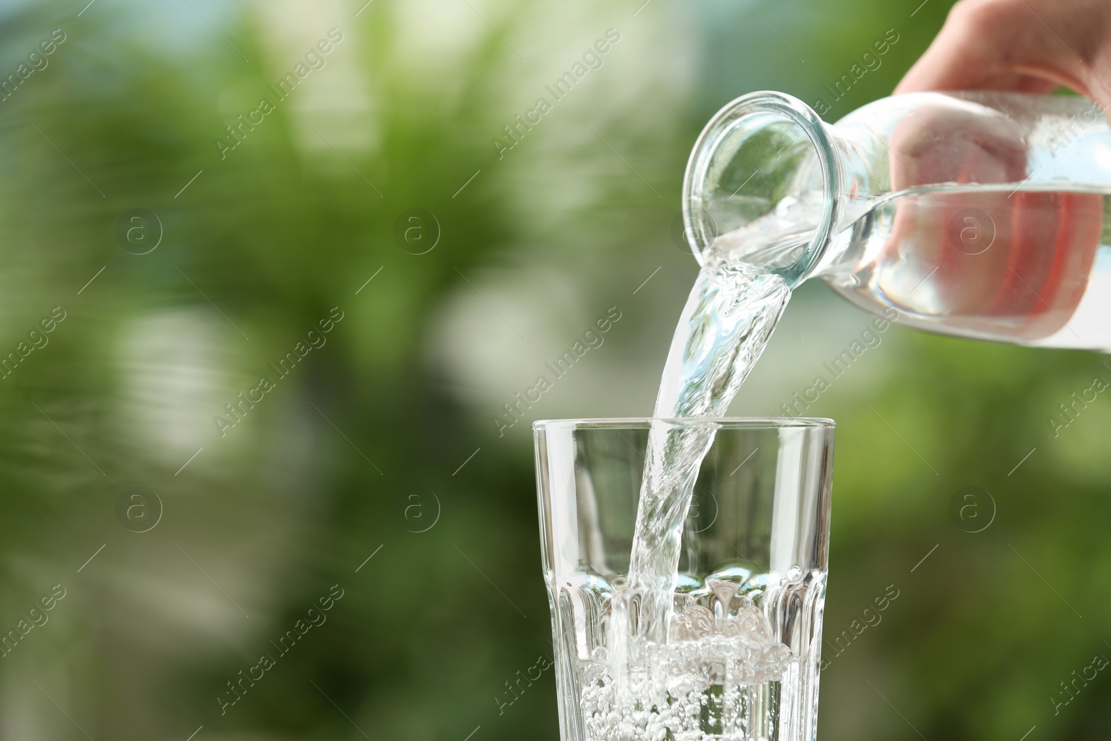 Photo of Woman pouring water from bottle into glass against blurred background, closeup. Space for text