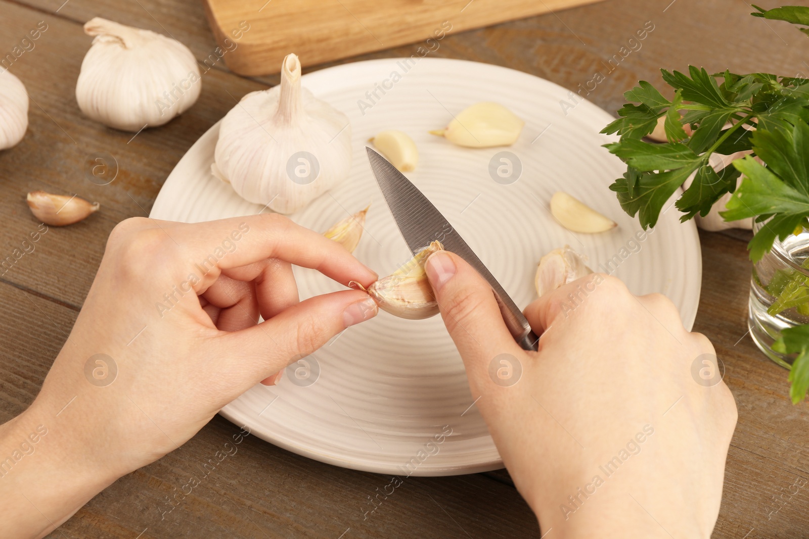 Photo of Woman peeling fresh garlic at table, closeup